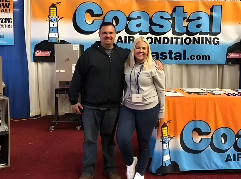 Two Coastal Air Conditioning representatives posing at a trade show booth